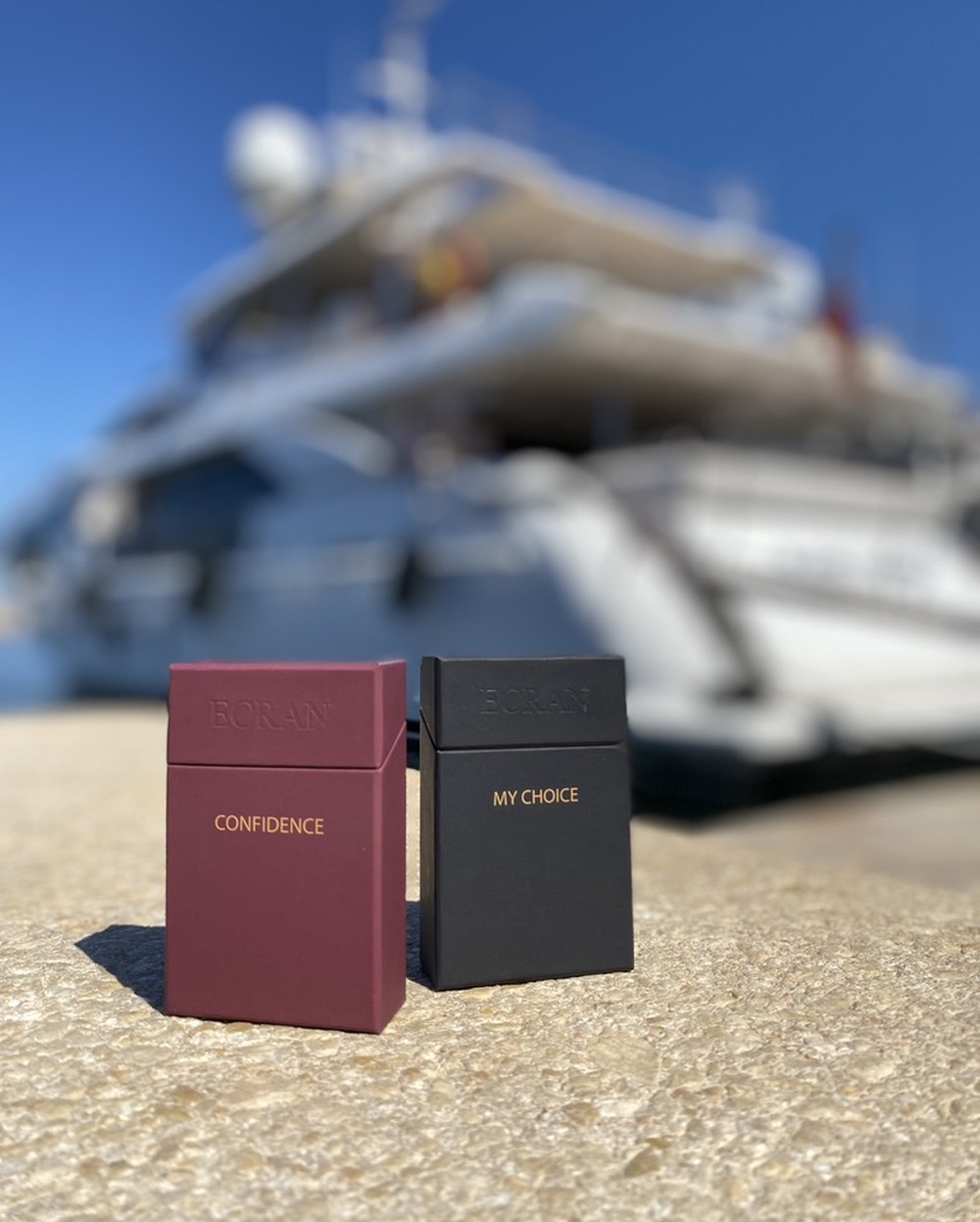 Étuis ÉCRAN Confidence et My Choice posés sur un ponton, yacht en arrière-plan